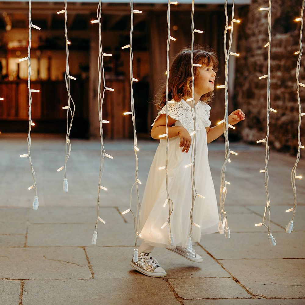 Flower girl runs through fairy lights curtain