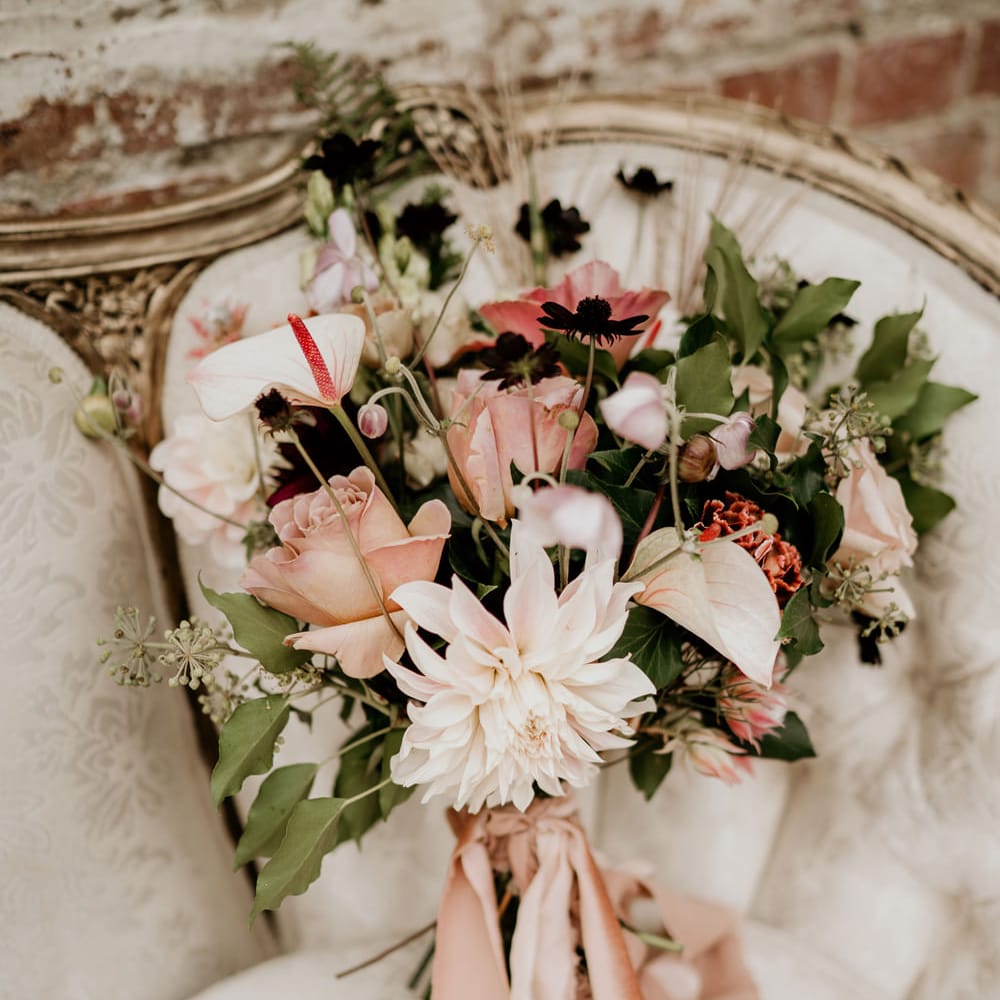 Romantic blush pink wedding bouquet resting on an ornate cream sofa tied with ribbon 