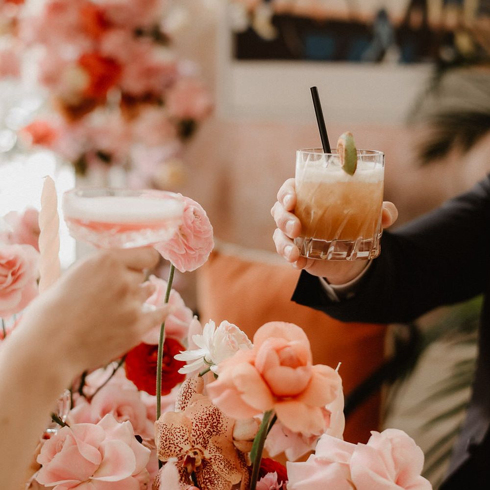Toasting with pink and peach cocktails over peach wedding flowers