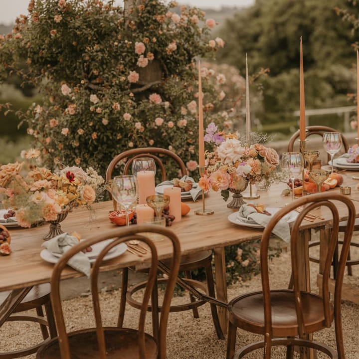 Outdoor wedding reception at Euridge Manor with orange taper candles, gold candlesticks, pastel orange and pink flowers and iridescent glassware