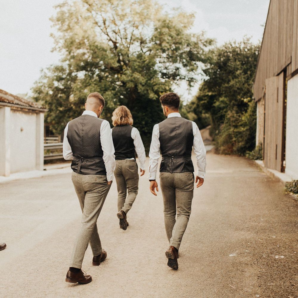 Three groomsmen and groom in sage green trousers, white shirts and silk backed waistcoats walk down country lane at Anran Devon 