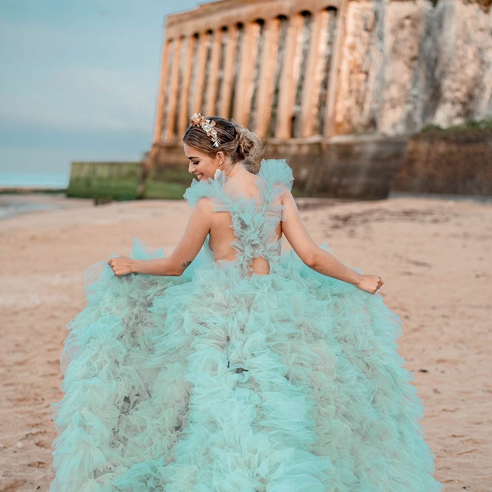 Bride in a layered tulle mint green wedding dress holding out her train on the beach 