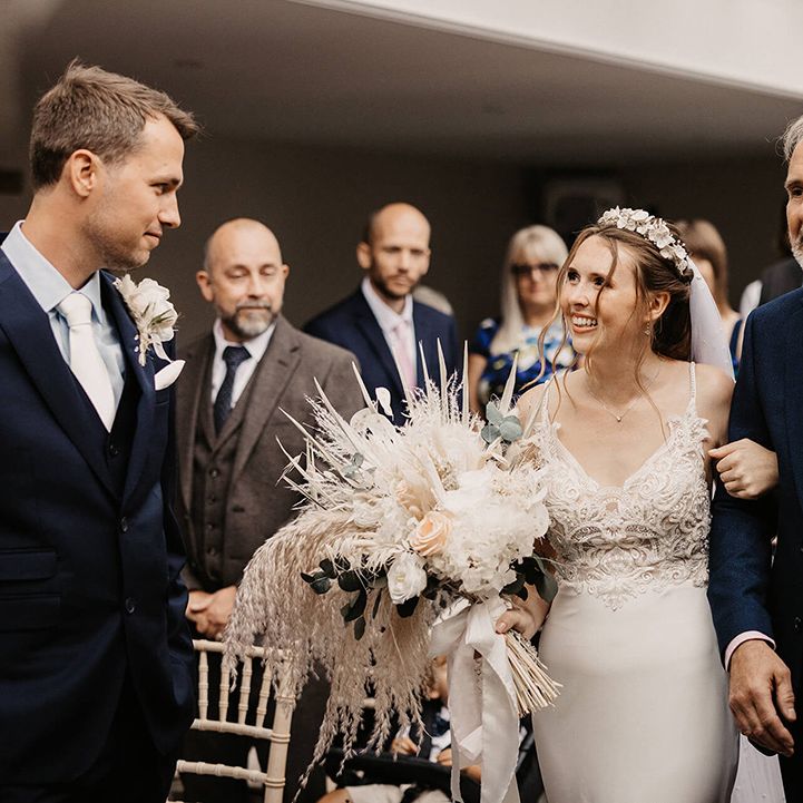Bride holds dried floral bouquet as she walks down the aisle with her father