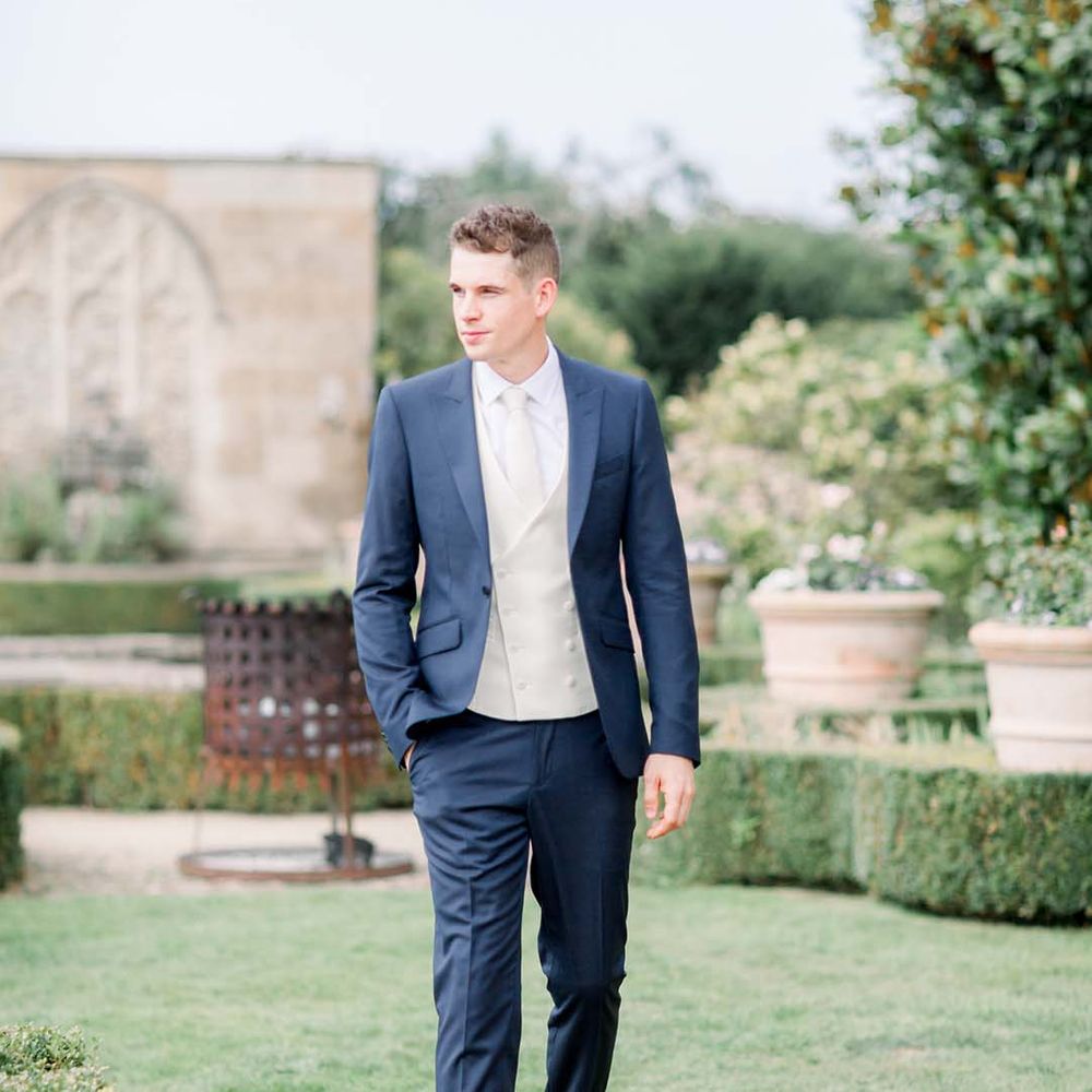 Groom wears wedding suit complete with white waistcoat and tie 