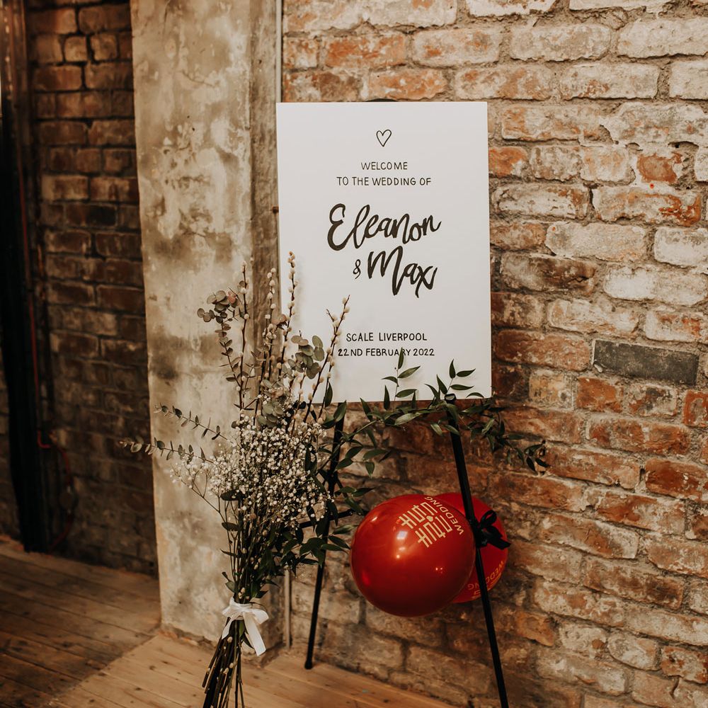 White rustic wedding welcome sign on black easel with dried florals and balloons for industrial style wedding