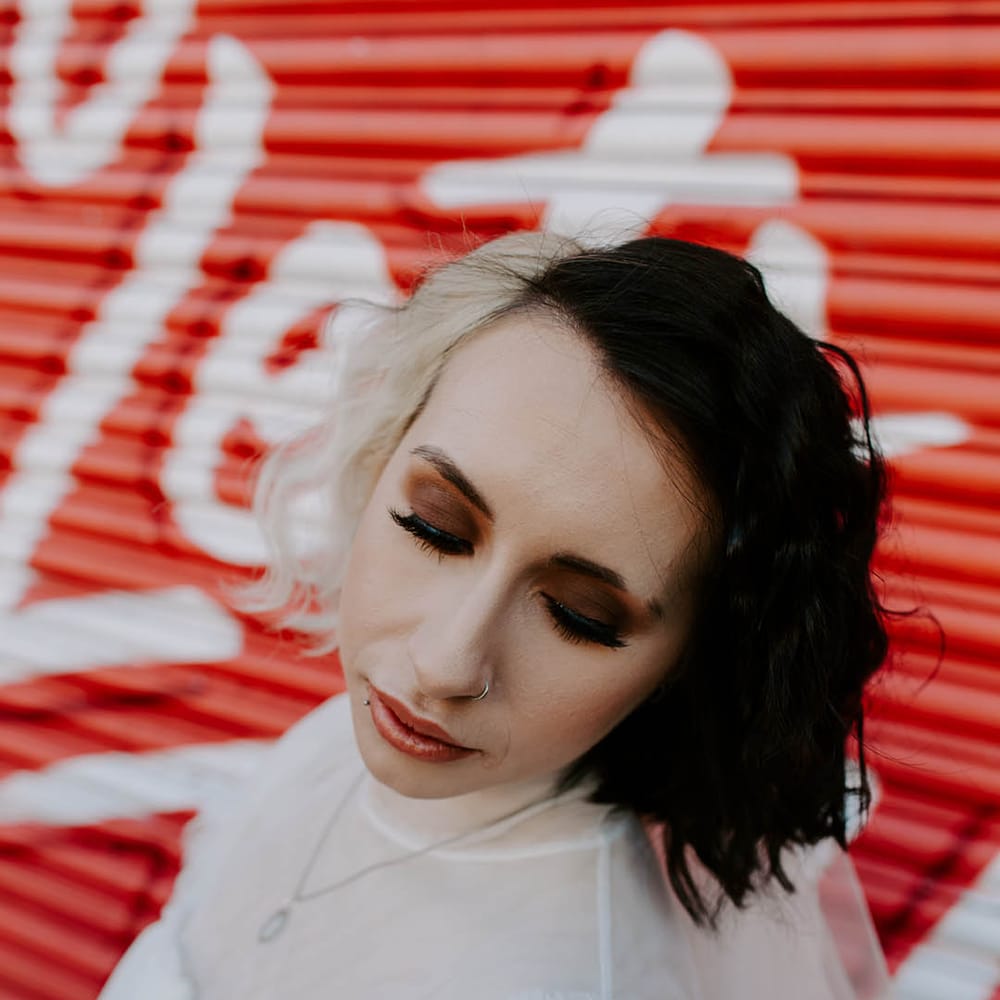 Bride in a tulle short wedding dress with high neck with two different toned hair, dark eye makeup and barely there lipstick 