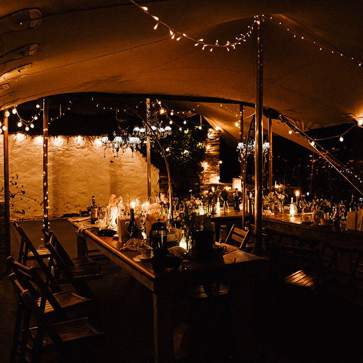 Fairy lights and candles decorate the outdoor reception area under canopy during the night time
