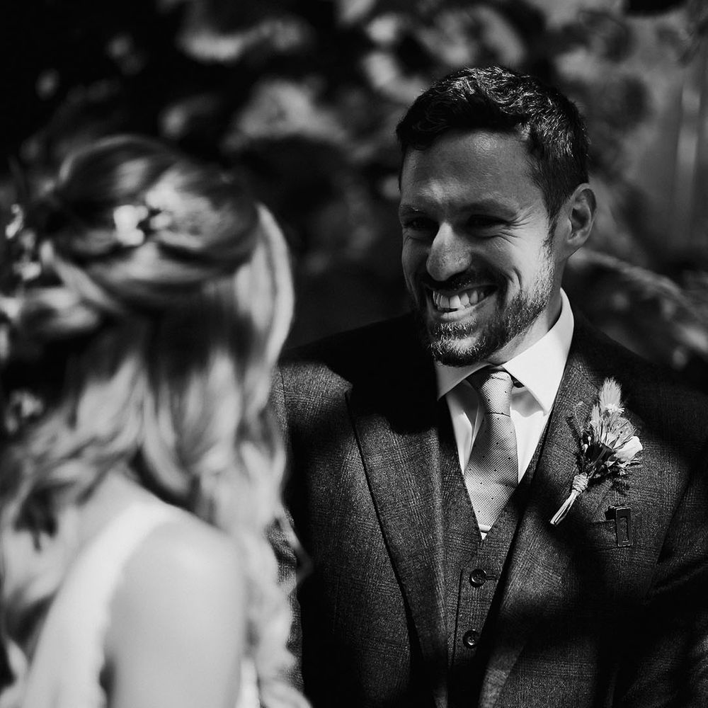 Groom in three piece suit and spotted tie smiling at the bride 