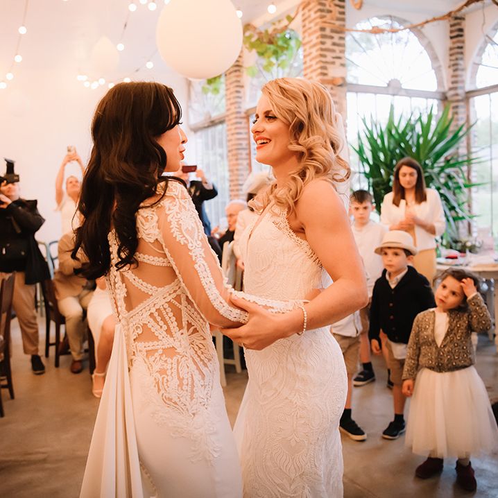 Brides share their first dance together while wedding guests watch 