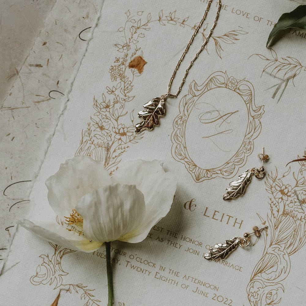 delicate leaf necklace and earrings resting on the vintage style wedding stationery 