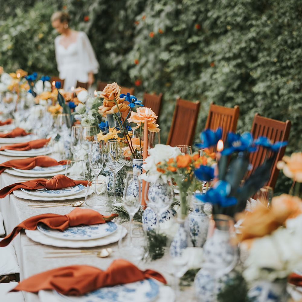Wedding table setting with orange taper candles, blue and white plates and vases with blue and orange flowers