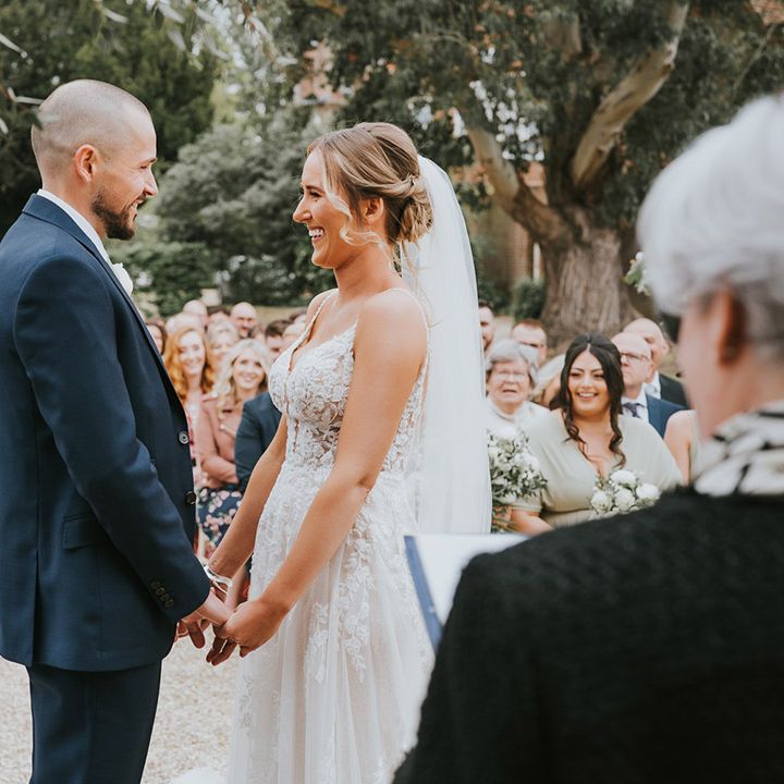 Bride in a floral lace wedding dress standing at the altar with the groom in a dark blue suit 