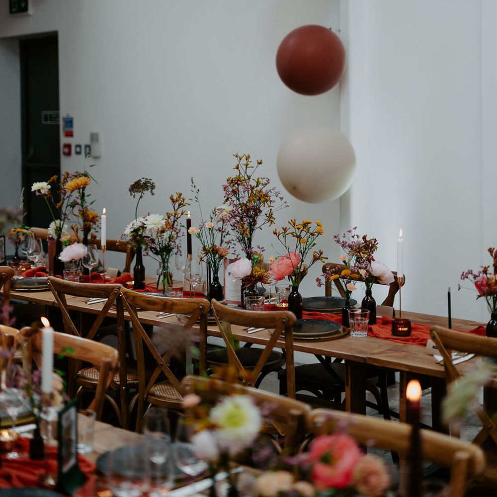 Retro coloured balloons and wooden banquet tables finished with orange table runner and small floral arrangement centrepieces 