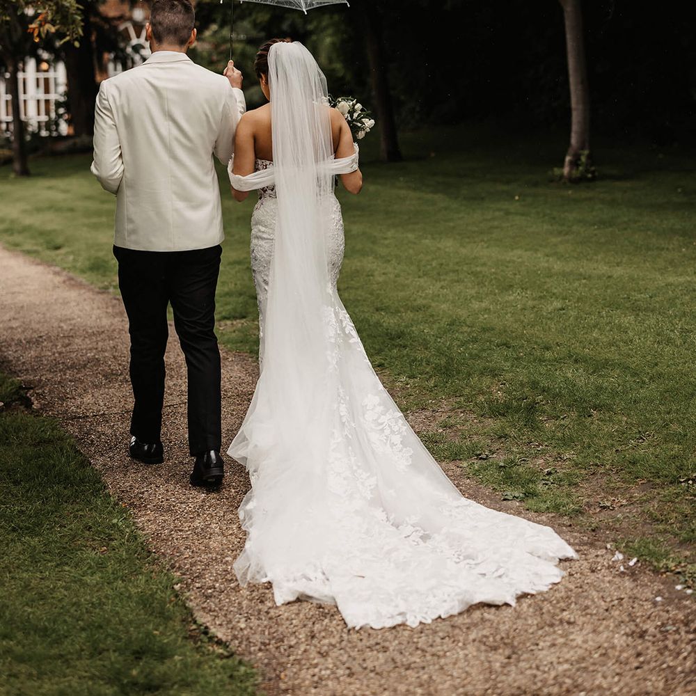 Bride and groom walk underneath an umbrella together on their wedding day at The Orangery in Kent 