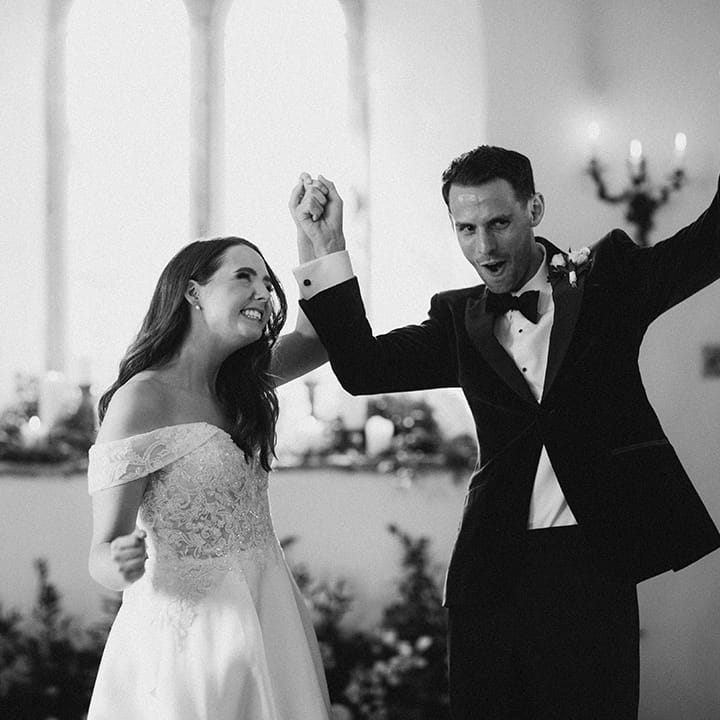 The bride and groom turn and face their wedding guests as they raise their arms in celebration 