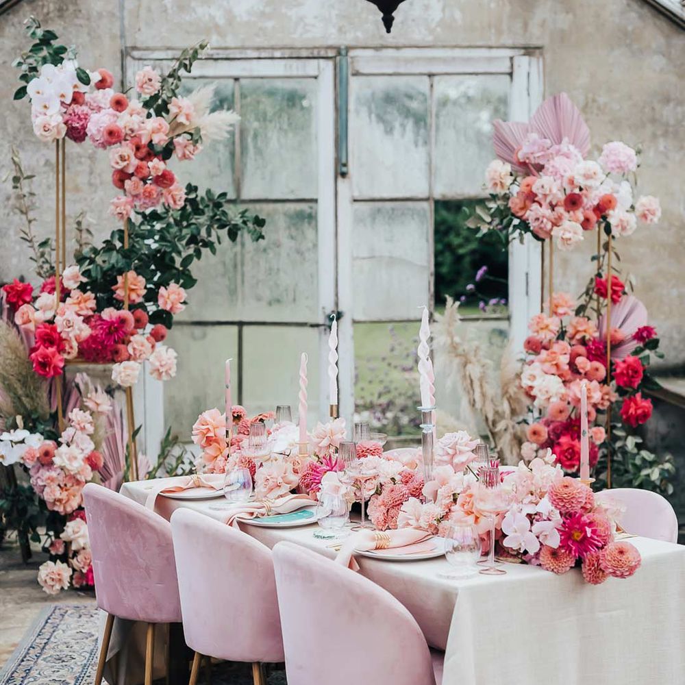 Opulent pink wedding tablescape with pink velvet chairs, large pink floral arrangements, pink twisted tapered candles and large black chandelier 