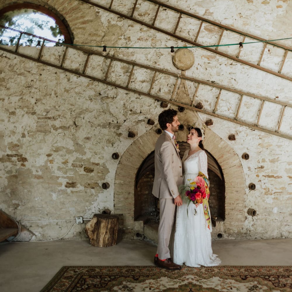 Bride and groom at rustic wedding venue in italy wearing a white lace wedding dress, boho bridal crown, and greige groom's suit