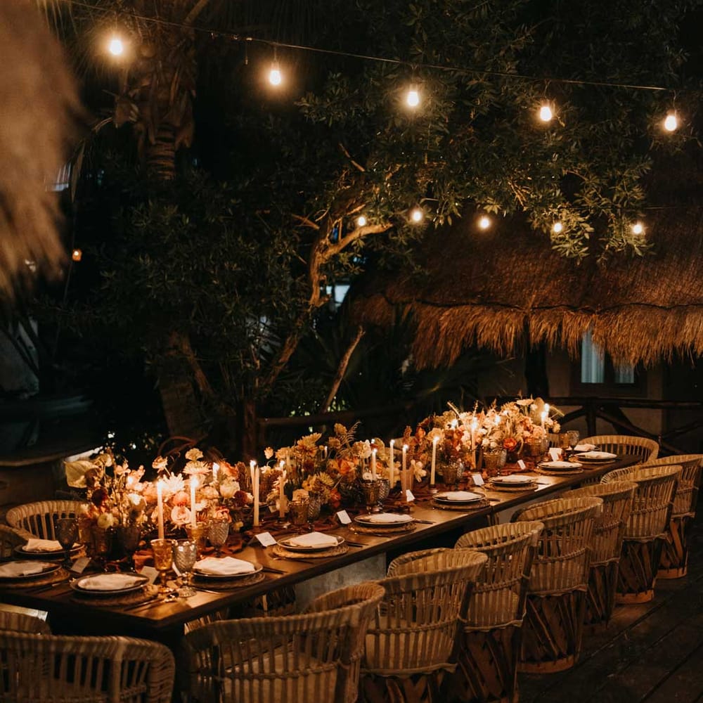 Rustic wedding tablescape by the Mexican sea with wicker chairs, burnt orange dried roses, dried flower and foliage floral centrepieces, wooden slate wedding table numbers, light orange tapered candles and burnt orange table runners
