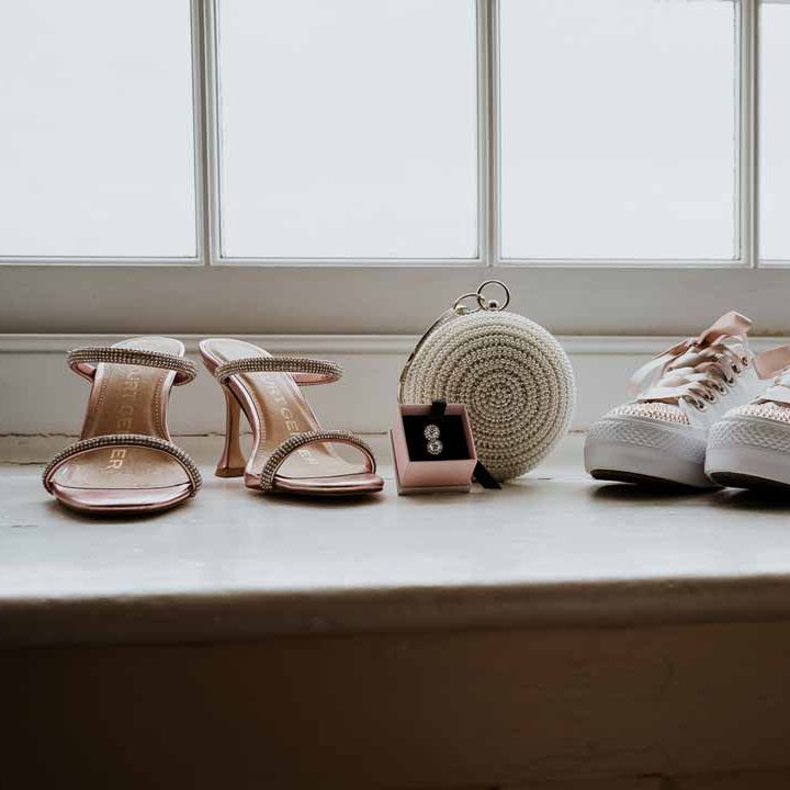 Rose gold open toe strappy Kurt Geiger wedding heels next to silver wedding jewellery, white wedding converse with rose gold details and Black Opium wedding scent 