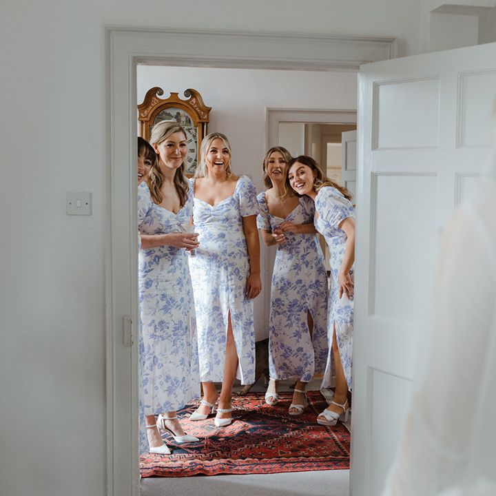 Bridesmaids in blue and white floral patterned bridesmaid dresses looking at the bride in her dress for the first time 