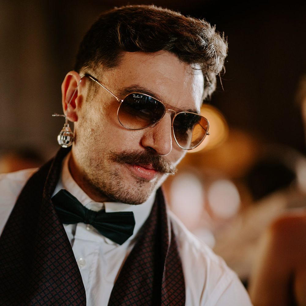 Groomsman wearing disco ball earrings and sunglasses at festival wedding 