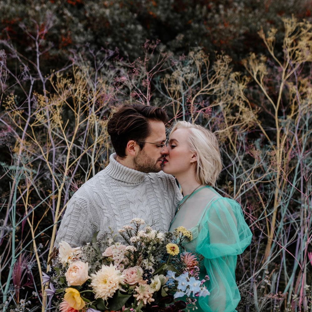 Groom in a grey turtle neck jumper kissing his bride in a pastel green sheer wedding dress on the beach 