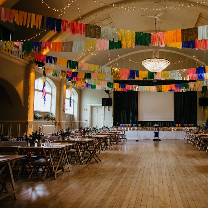 DIY Village hall wedding with wooden tables and colourful Streamers hanging from the ceiling 