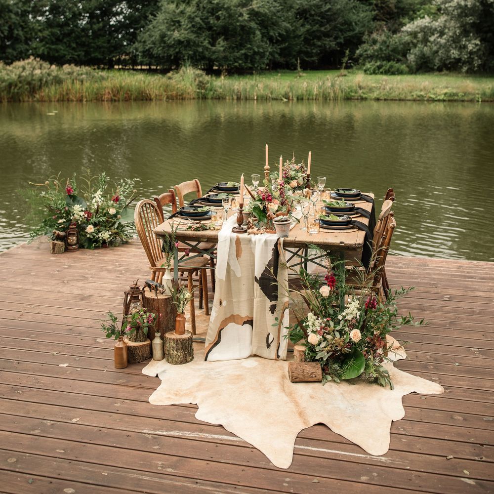 Wooden table sits on dock in front of lake with camouflage table runner