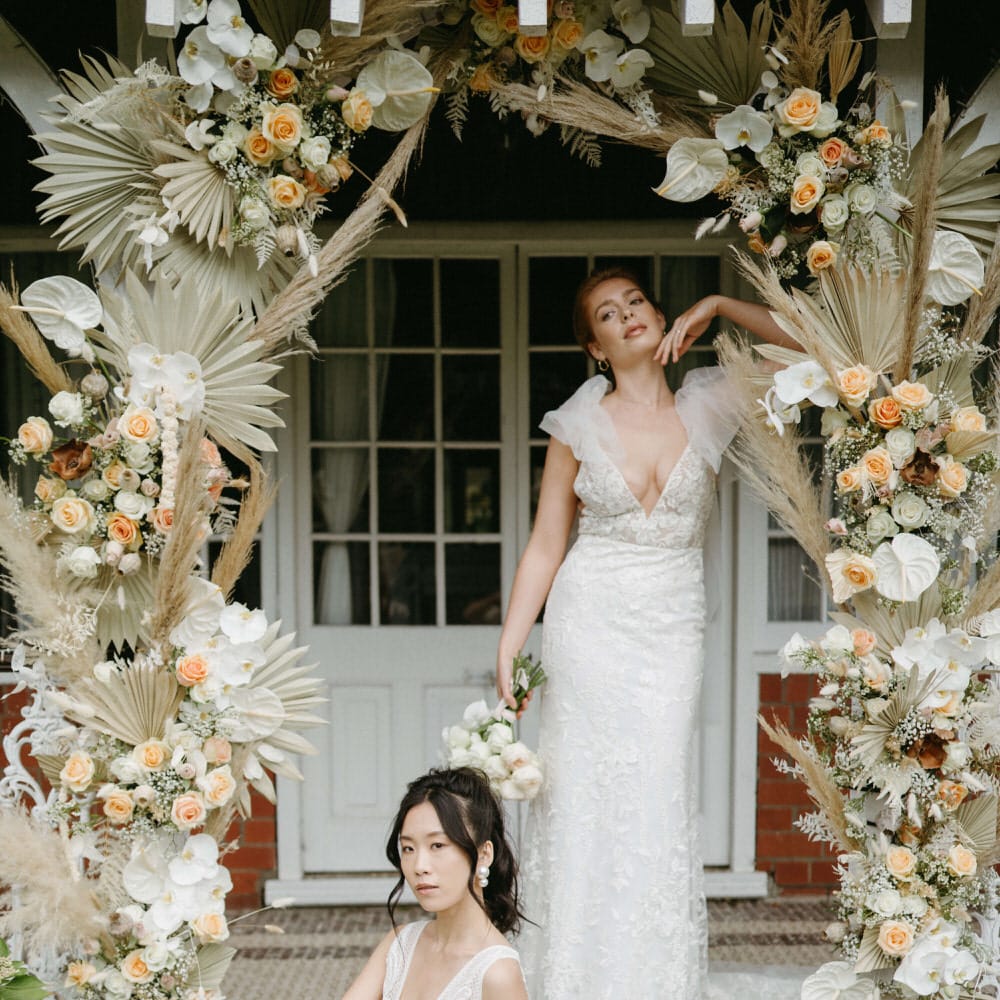Two brides at Berwick lodge under boho flower arch, wearing boho inspired plunge neck tulle wedding dresses with floral detail