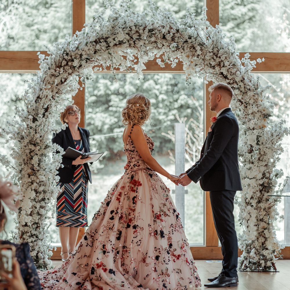 Bride & groom stand beneath floral arch during wedding ceremony