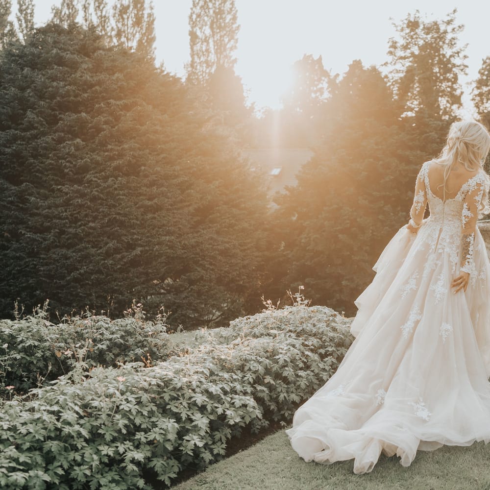 A blonde bride walks away from the camera in long tulle layered wedding dress as the sun sets.
