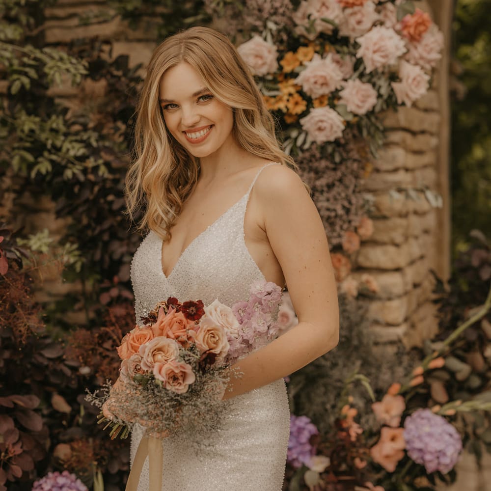 Beautiful bride in a sequin Made With Love strappy dress holding an pastel orange, peach and coral wedding bouquet 