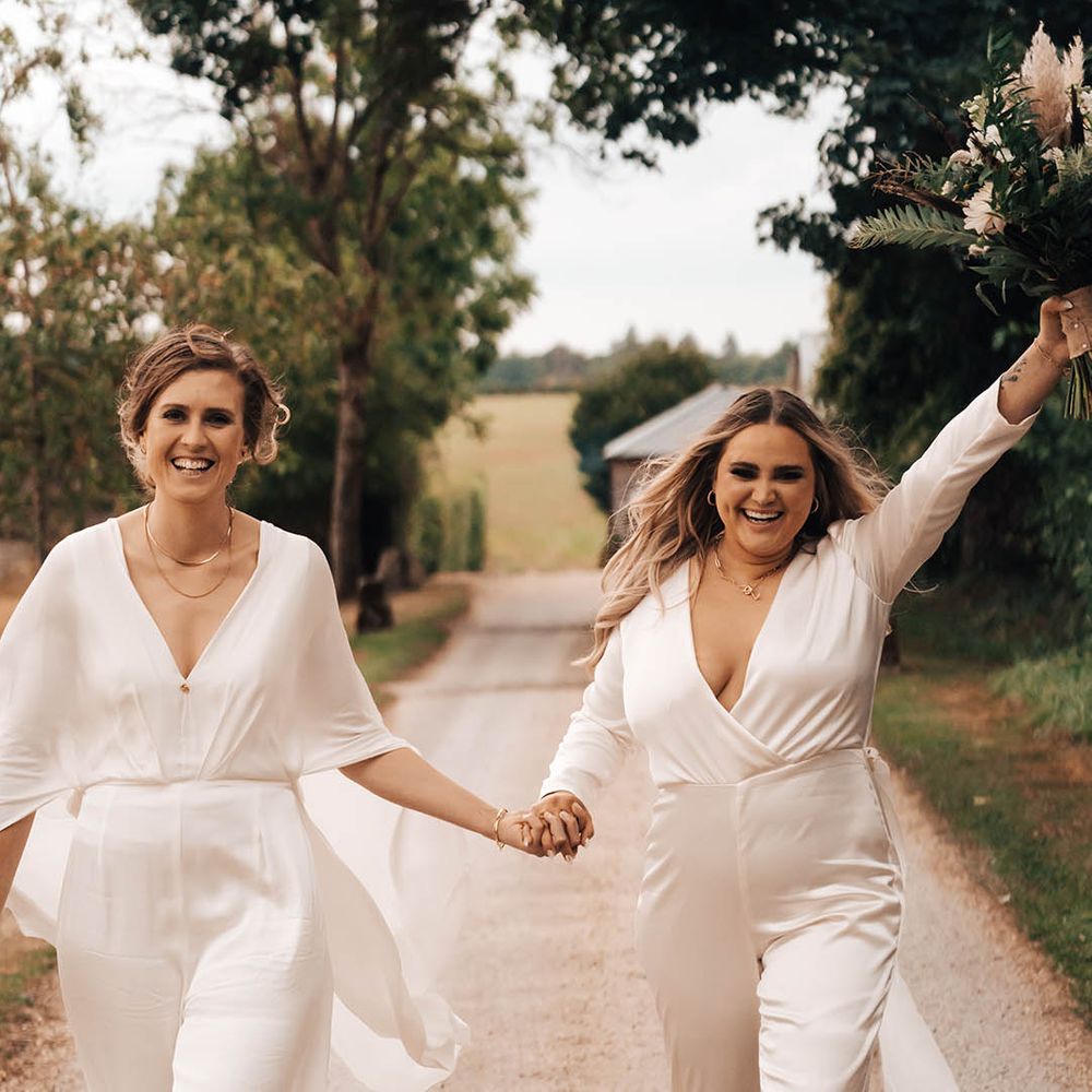 Blonde bride lifts her hand in the air in celebration as she holds hands with her wife on wedding day