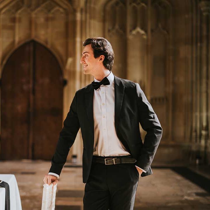 Groom in a black suit and bow tie standing at the intimate reception table decorated with black, white and gold tableware and flowers 
