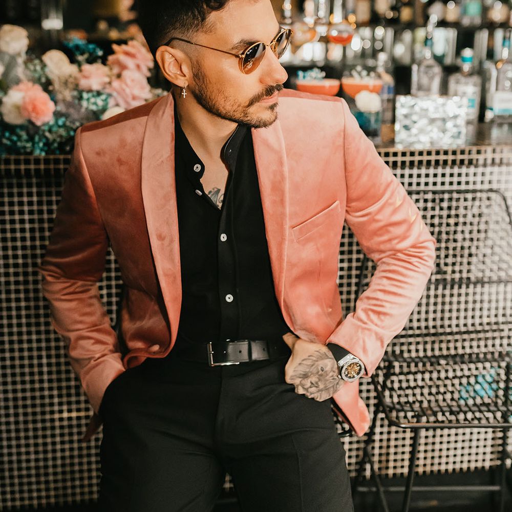 Stylish groom sitting at the bar in a black shirt, pink velvet jacket and sunglasses 