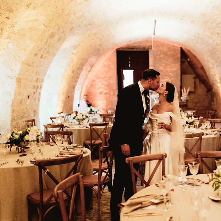 Bride & groom kiss in wedding venue for reception surrounded by classic white floral bouquets with green foliage