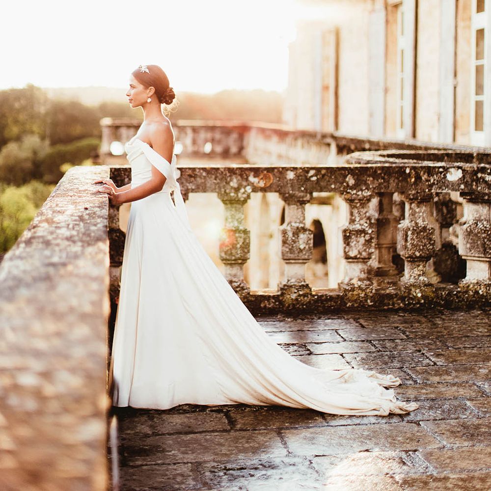 Bride stands on balcony as the sun shines behind her on her wedding day