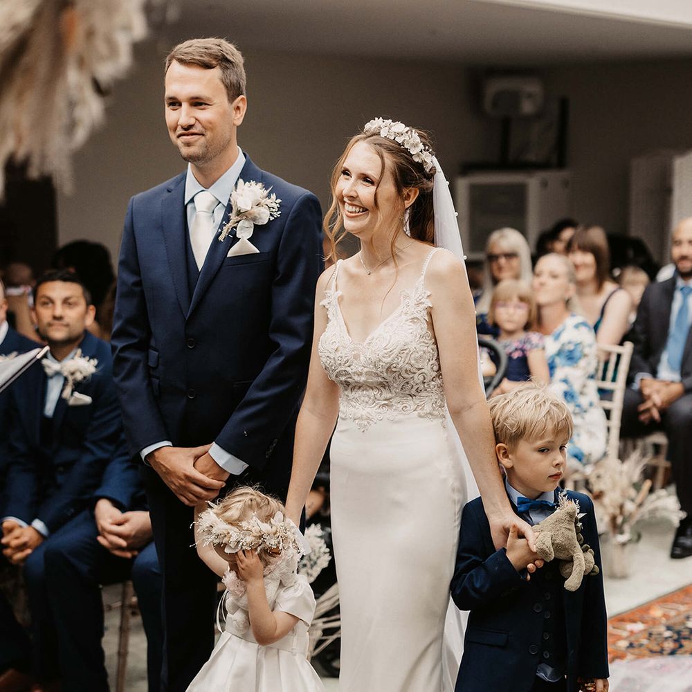 Bride & groom stand together with their daughter and son on their wedding day