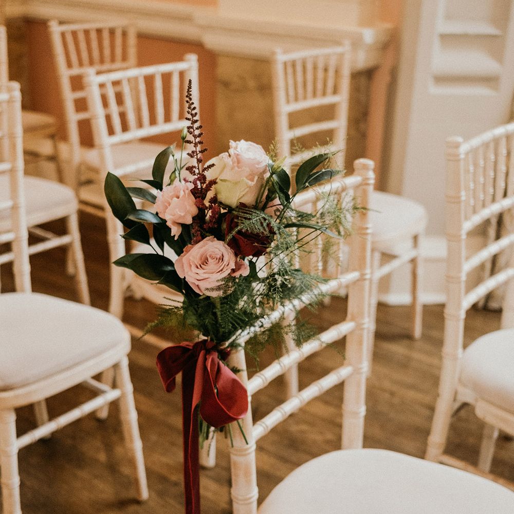 Pink flower chair decor tied with burgundy velvet ribbon at winter wedding