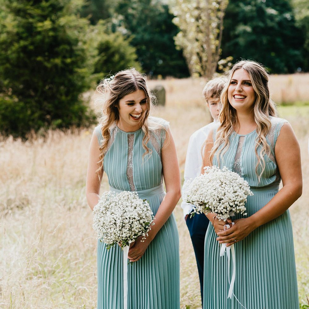 Bridesmaids in green pleated dresses with sheer lace panel inserts hold white gypsophila wedding bouquets with half up half down hair