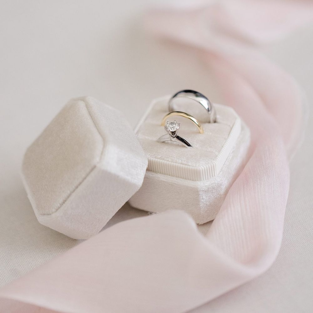 Wedding rings sit in white velvet box beside pink fabric 