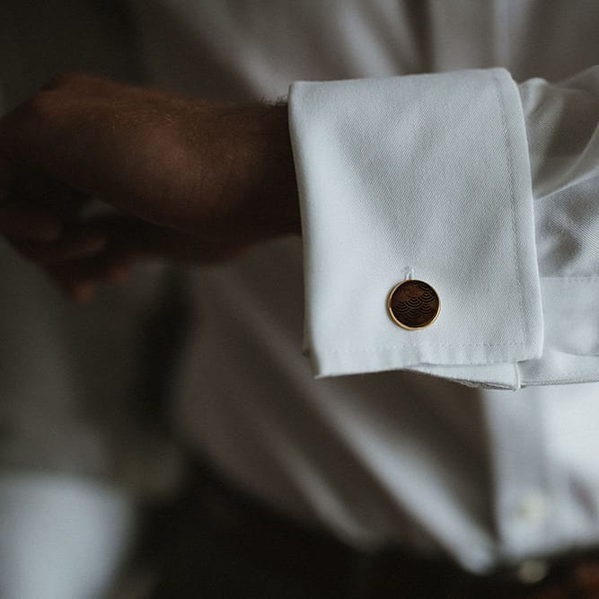Groom wears gold cufflinks with engraved pattern to the middle 