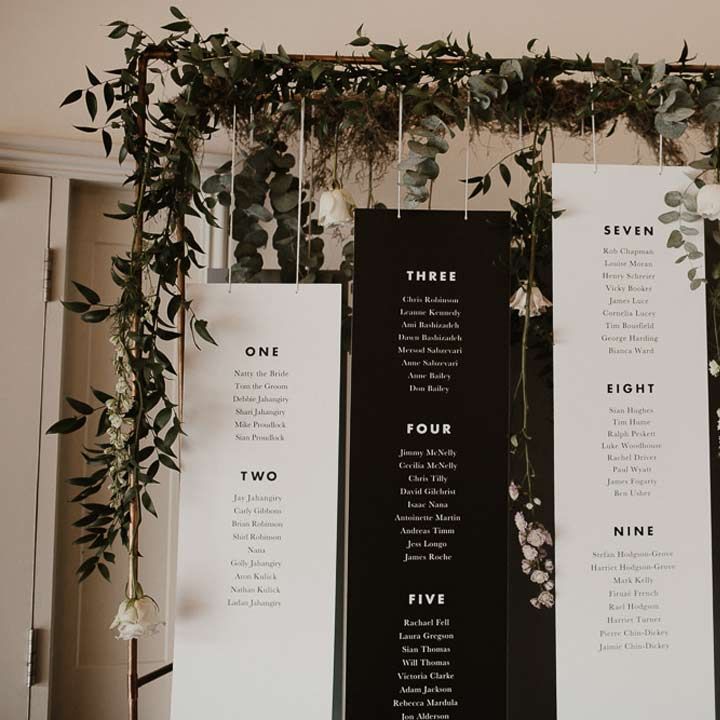 Four hanging monochrome table plan signs with greenery and fauna hanging around them