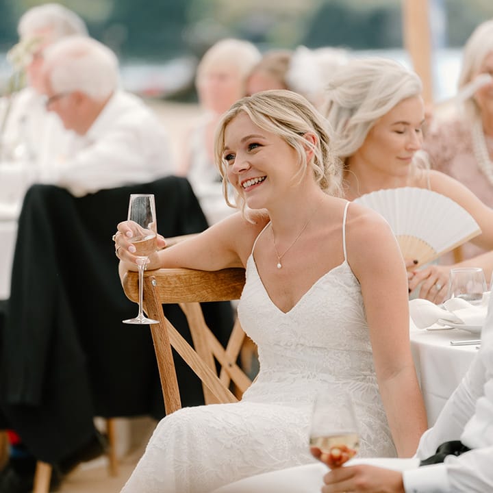 Bride wearing fitted lace wedding dress sits beside her groom during outdoor wedding reception 