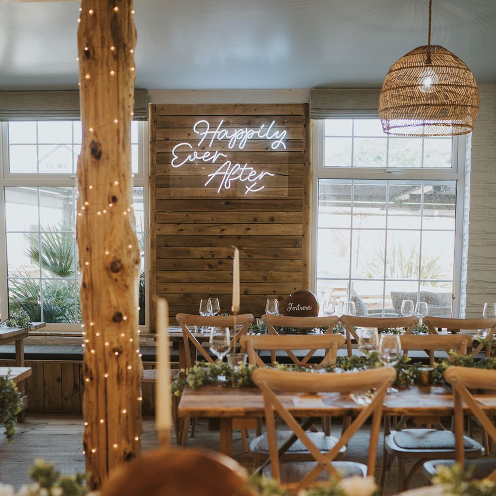 Neon wedding sign on wooden wall in rustic reception setting with green foliage table runners 