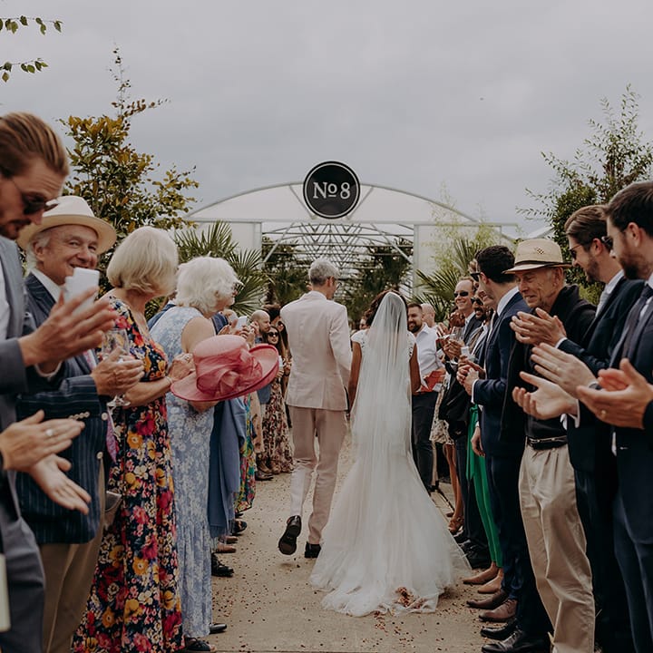 Bride and Groom walk between clapping guests towards Architectural Plants venue