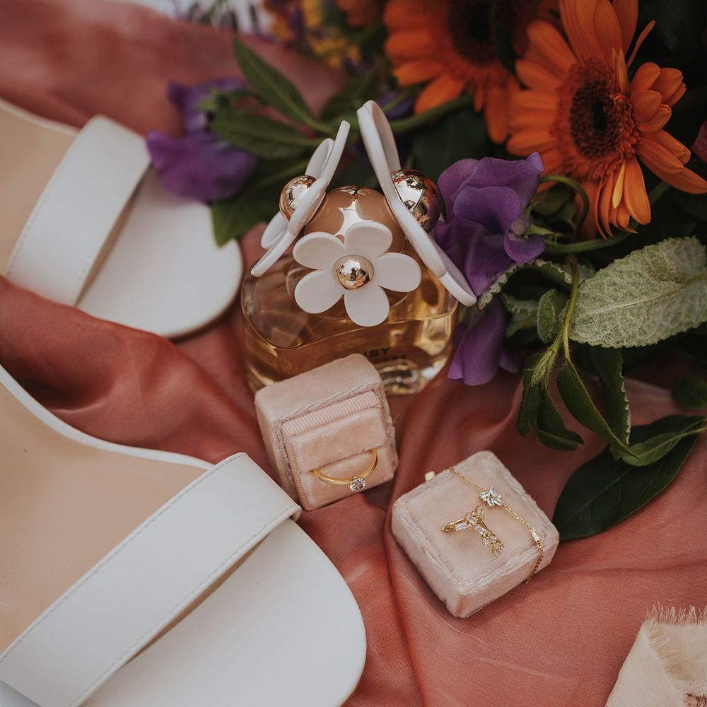 Wedding ring and jewellery beside Marc Jacobs perfume and white wedding shoes 