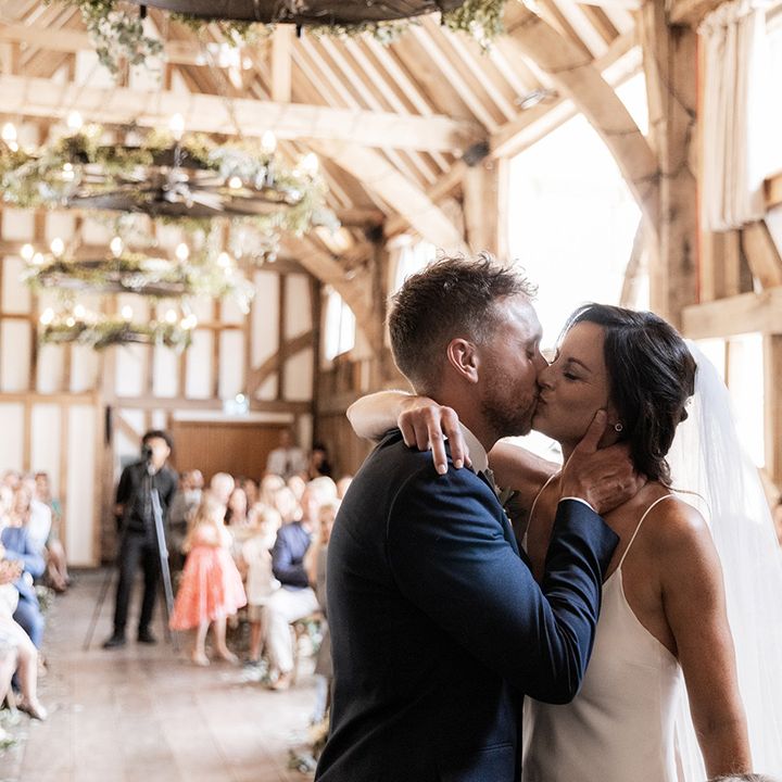 Bride in Grace Loves Lace wedding dress kisses her groom during rustic barn civil ceremony 