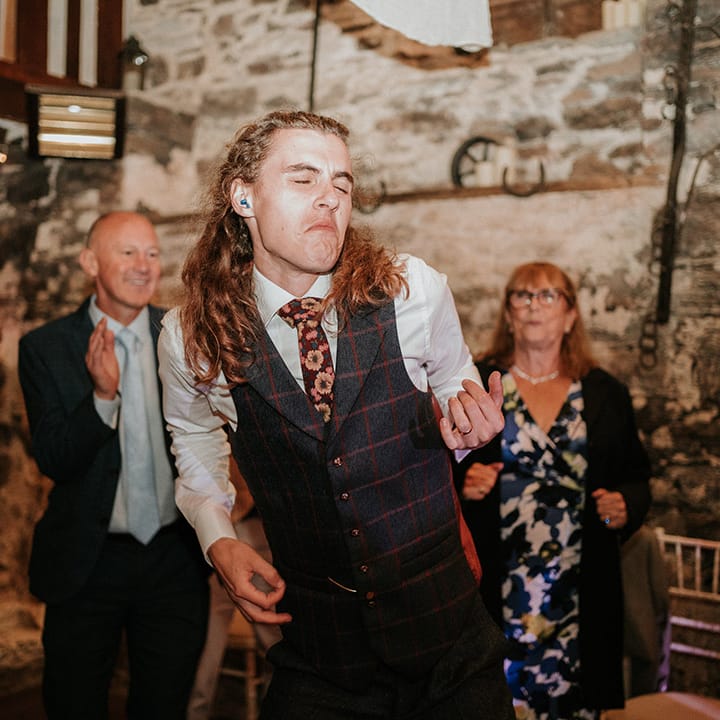 Groom in dark grey checkered waistcoat with burgundy flower patterned tie dancing to live wedding music at boho wedding 