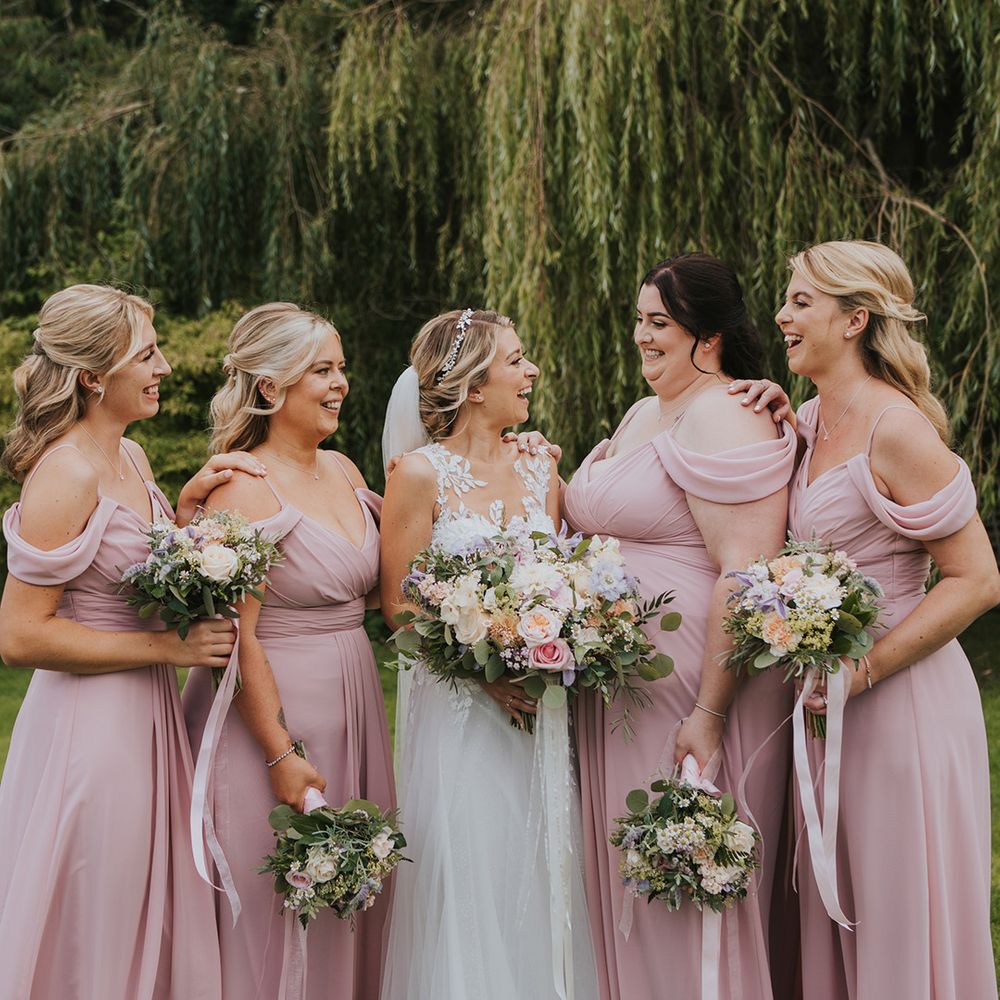 Bridesmaids in pink off the shoulder bridesmaid dresses with the bride in a lace and tulle wedding dress 
